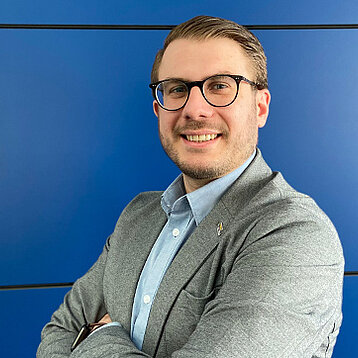 Lars Intraschak, Verkaufs-Außendienst, steht vor einer blauen Wand
