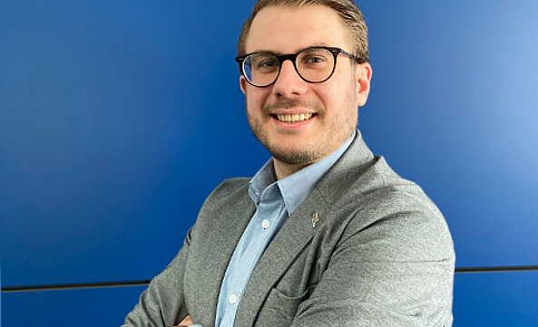 Lars Intraschak, Verkaufs-Außendienst, steht vor einer blauen Wand