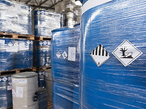 gestapelte Paletten mit blauen Fässern mit Gefahrstoff-Symbolen sind mit Folie verpackt