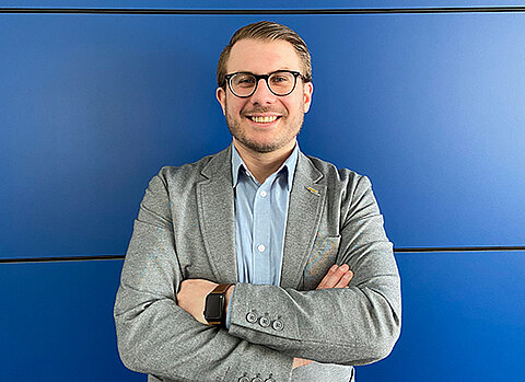 Büromitarbeiter mit Brille von Streck Transport steht vor einer blauen Wand