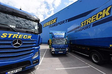 Drei Lkws von Streck Transport stehen auf dem Betriebsgelände in Freiburg vor der blauen Halle