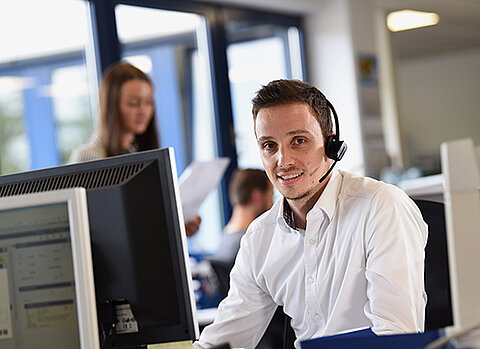 Ein Mitarbeiter von Streck Transport mit Headset sitzt im Büro an seinem Schreibtisch und bedient einen Computer