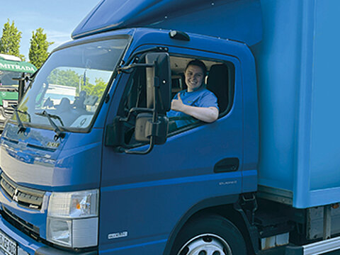 Eine Auszubildende von Streck Transport fährt einen blauen Hybrid-Lkw am Standort Freiburg