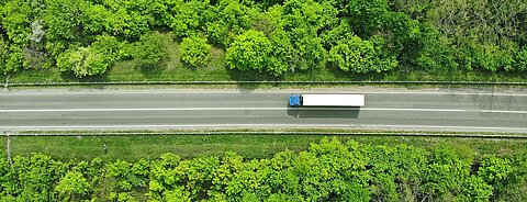 Ein Lkw ist von oben zu sehen, wie er auf einer geraden Straße durch den Wald fährt