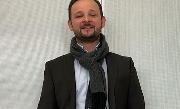 Verkaufs-Außendienst-Mitarbeiter Kevin Stange steht vor einer weißen Wand des Streck Transport-Kundenzentrums in Freiburg