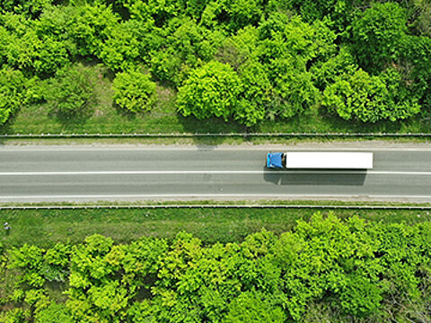 Ein Lkw ist von oben zu sehen, wie er auf einer geraden Straße durch den Wald fährt