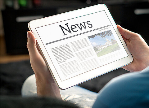 Zwei Hände halten ein Tablet, auf dem groß das Wort News zu lesen ist