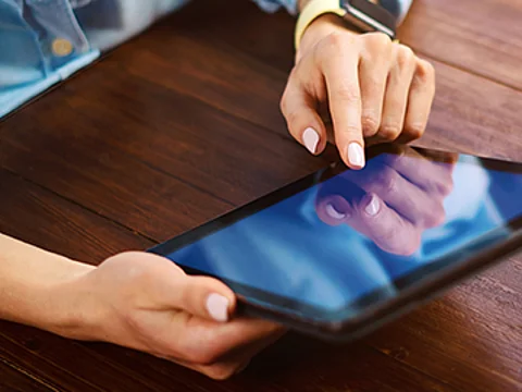 Hände einer Frau an einem Tisch, die ein Tablet bedienen
