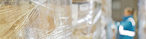 Eine Mitarbeiterin von Streck Transport steht zwischen Paletten, auf denen Ware, die transportiert werden soll, in Plastikfolie eingepackt ist
