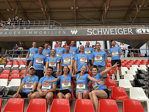 Die 16 Kolleginnen und Kollegen aus dem Team Streck sitzen vor dem Firmenlauf B2Run Freiburg auf der Tribüne des Europa-Park-Stadions und lachen in die Kamera