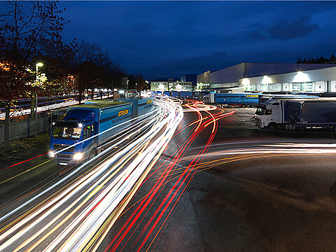Lkws fahren bei Nacht mit eingeschalteten Scheinwerfern über das Betriebsgelände von Streck Transport in Freiburg