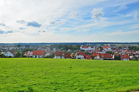 Ansicht der Stadt Meßkirch bei leicht bewölktem Himmel, im Vordergrund eine grüne Wiese, im Hintergrund Gebäude und eine Kirche