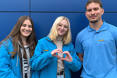 Drei junge Auszubildende in Arbeitskleidung von Streck Transport lachen in die Kamera