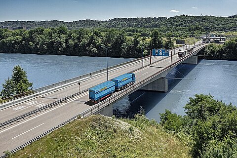 Blauer Streck-Lkw überquert eine Brücke über den Fluss Rhein, im Hintergrund ein Grenzübergang zur Schweiz
