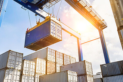 Ein Kran bewegt einen Schiffscontainer im Hafen bei Sonnenschein