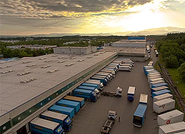 Luftbild der Umschlaghalle von Streck Transport in Freiburg mit vielen Lkws, die an Laderampen stehen, im Hintergrund der Schwarzwald
