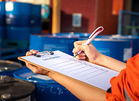 Eine Mitarbeiterin füllt im Lagerbereich mit dem Kugelschreiber eine Checkliste aus