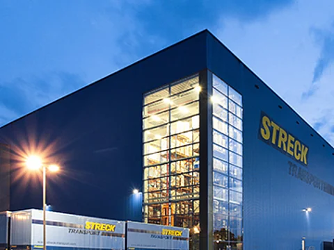 Die beleuchtete blaue Halle von Streck Transport in Freiburg mit Wechselbrücken in der Abenddämmerung