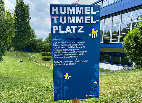 Ein Schild mit der Erklärung zum Hummel-Tummel-Platz vor dem Kundenzentrum von Streck Transport in Freiburg
