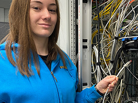 Eine Auszubildende zur Fachinformatikerin von Streck Transport steht vor einem Schaltschrank mit vielen Kabeln