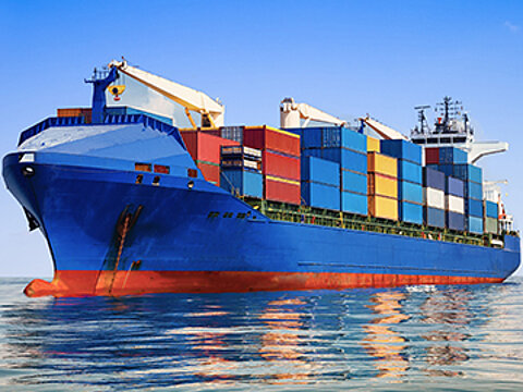 Ein blaues Schiff beladen mit Containern fährt bei ruhiger See und blauem Himmel auf dem Meer