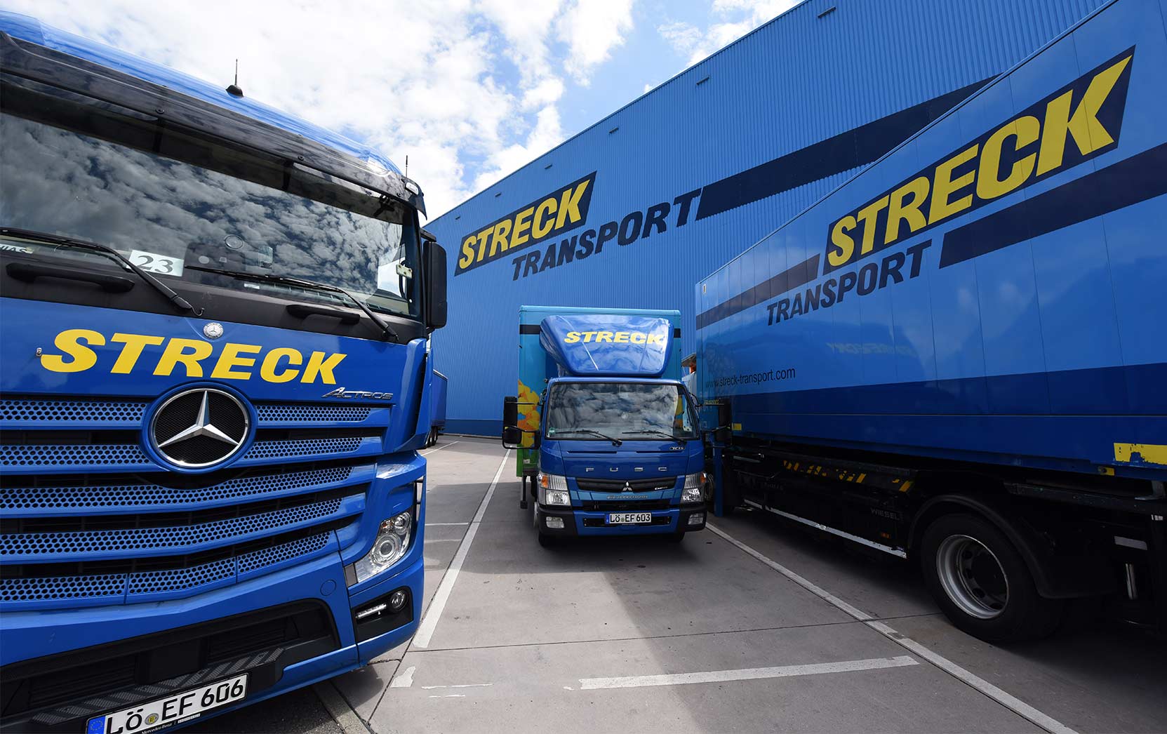 Drei Lkws von Streck Transport stehen auf dem Betriebsgelände in Freiburg vor der blauen Halle