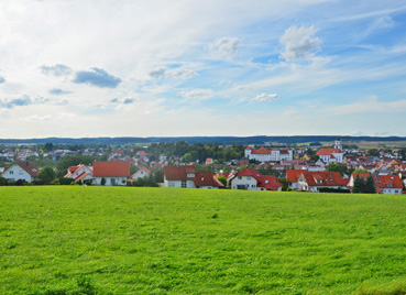 Ansicht der Stadt Meßkirch bei leicht bewölktem Himmel, im Vordergrund eine grüne Wiese, im Hintergrund Gebäude und eine Kirche