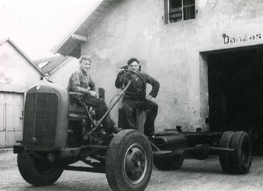 Zwei Männer sitzen im Jahr 1946 auf dem Fahrgestell eines Lkws und lachen