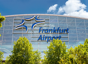 Außenansicht eines Terminals am Flughafen in Frankfurt am Main mit dem Logo Frankfurt Airport und Bäumen im Vordergrund