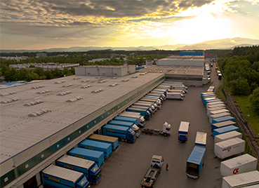 Luftbild der Umschlaghalle von Streck Transport in Freiburg mit vielen Lkws, die an Laderampen stehen, im Hintergrund der Schwarzwald