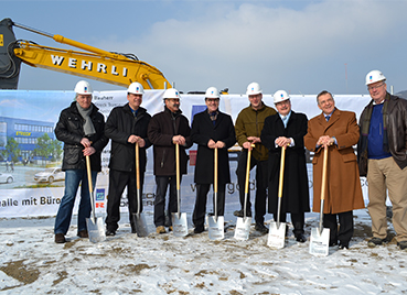 Gruppe von Männern mit Schutzhelmen und Spaten bei einem Spatenstich für Bauarbeiten von Streck Transport Schweiz