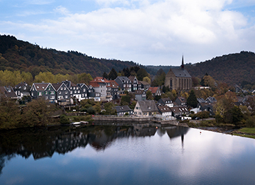 Blick auf einen Stadtteil von Wuppertal mit einer Kirche, im Vordergrund ein See, im Hintergrund Wald